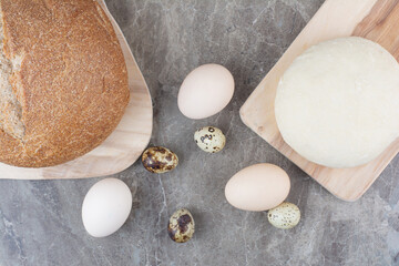 Chicken eggs with quail eggs and bread on marble background