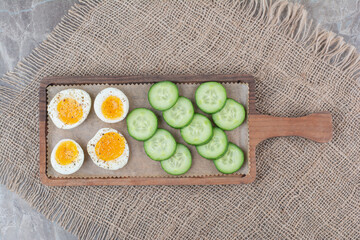 Sliced boiled eggs with cucumber on wooden board