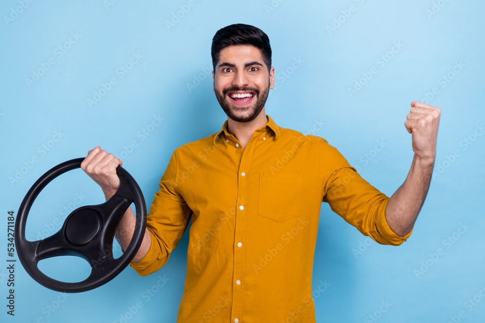 Poster Photo of delighted funny person raise fist success achievement hand hold wheel isolated on blue color background