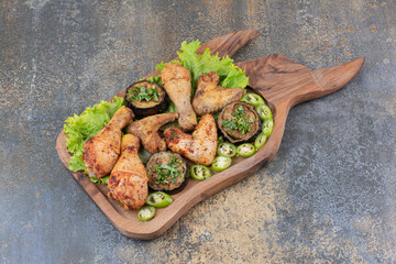 Roasted chicken legs and wings on wooden board with lettuce and pepper