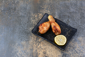 Grilled chicken drumsticks on black plate with lemon