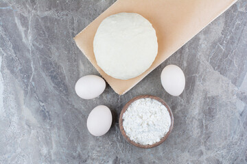 Dough with flour and chicken eggs on marble background