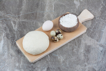Chicken egg with quail eggs and dough on wooden board