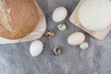 Chicken eggs with quail eggs and bread on marble background