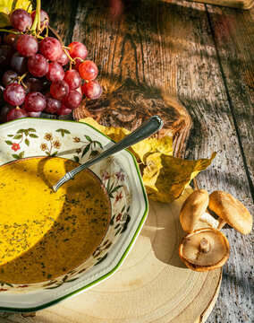 Close-up of a plate with pumpkin soup and mushrooms, bunch of grapes decorate the image. Wooden background, warm colors.
