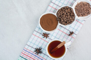 Cup of tea with coffee beans, ground coffee and cloves on tablecloth