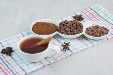Cup of tea with coffee beans, ground coffee and cloves on tablecloth