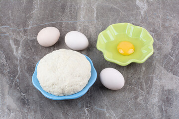 Dough on wooden board with green plate of raw egg