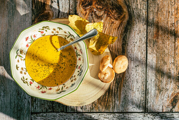Top view of a plate with pumpkin soup and mushrooms, wooden background, warm colors.