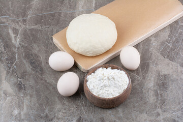 Dough with flour and chicken eggs on marble background