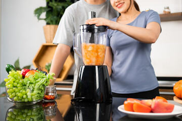 Crop image of happy Asian couple enjoy using blender machine for making healthy vegan smoothie on the kitchen counter. Couple making vegan smoothie together at home for a healthy lifestyle.