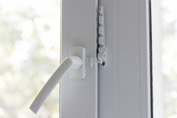 Close-up of a white pvc balcony door handle, an insulating glass window comb fixes the sash. Fittings for child protection and safe ventilation