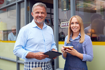 Obraz premium Portrait Of Male And Female Owners Or Staff Standing Outside Coffee Shop With Digital Tablet