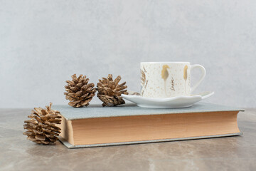 Cup of aromatic coffee on top of book with pinecones