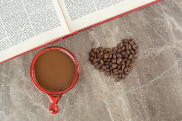 Coffee on marble surface with coffee beans formed like heart and book