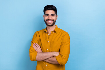 Photo of smart brunet millennial guy crossed arms wear yellow shirt isolated on blue color...