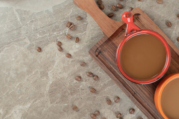 Two cups of coffee on wooden board with coffee beans