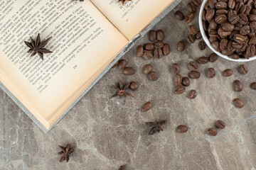 Bunch of coffee beans scattered on book with cup of beans