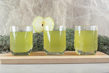 Three glasses of juice with apple slice on wooden board
