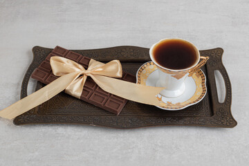 Cup of espresso with chocolate bar tied with ribbon on tray
