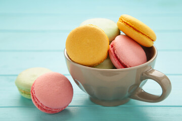 French macarons in cup on blue wooden background.