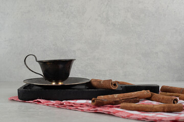 Cup of coffee with cinnamon sticks on dark board