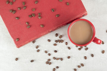 Red cup, coffee beans and book on marble background