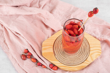Glass of fresh lemonade with rosehips on wooden plate