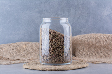 Jar full of brown lentil sitting on a trivet on marble background