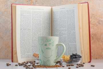 An opened book with cup and coffee beans on marble background