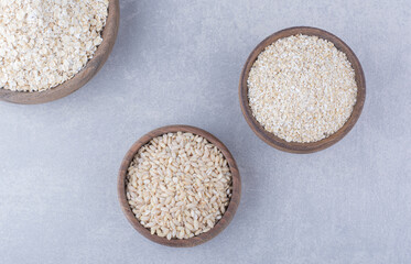 Small bowls filled with rice, oat and oat flakes on marble background