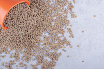 Bucket of brown lentil spilled all over marble background