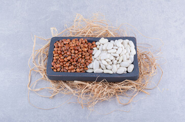 Small tray placed on a pile of straw, filled with red beans and navy beans on marble background