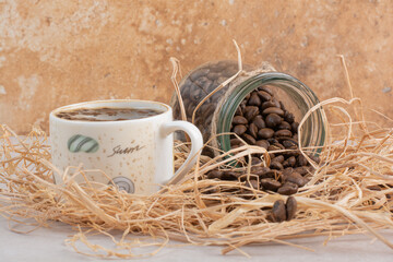 A cup of aroma coffee with jar full of beans on hay