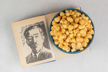 Platter of caramel coated popcorn resting on a book with a portrait on marble background