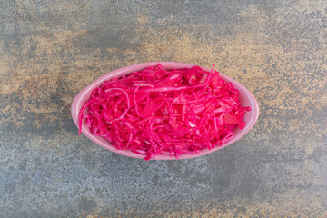 A pink plate full of red salty cabbage on marble background