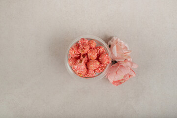 Two corollae of pink rose and a glass bowl of popcorn on marble background