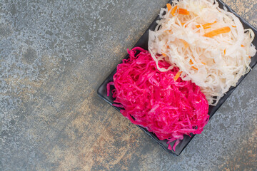 A dark plate full of red salty cabbage on marble background