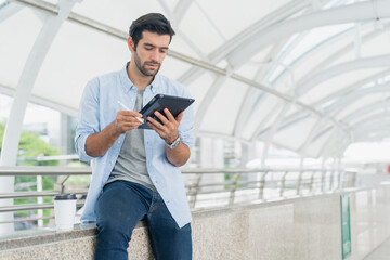 Young man using smart phone working and video conference meeting at outdoor. Young creative man looking at screen typing message with tablet.Handsome young man using digital tablet