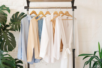 Trendy capsule wardrobe in beige and light blue on a rail rack against the background of a white...