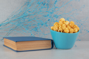 Blue branches, a bowl of caramel coated popcorn and a book on marble background