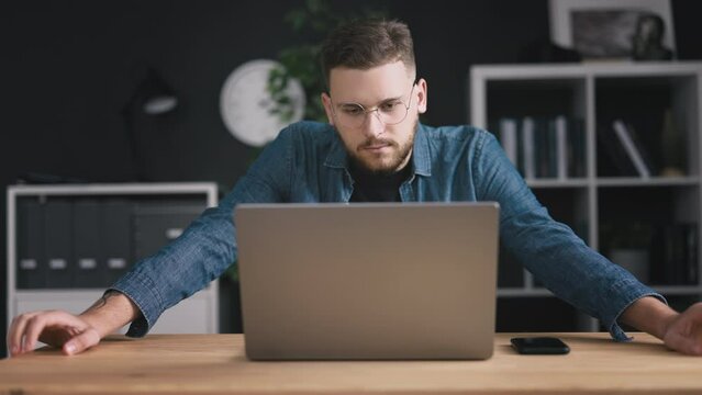 Young bearded man, thoughtful programmer at desk with laptop, thoughts and idea, brainstorming