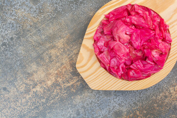 A wooden plate full of red salty cabbage on marble background