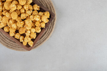 Wooden platter on a trivet filled with flavored popcorn on marble background