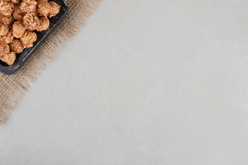 Black platter on a piece of fabric, holding a portion of flavored popcorn on marble background