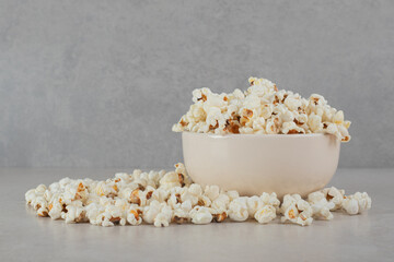 Crispy popcorn inside and around a white bowl on marble background