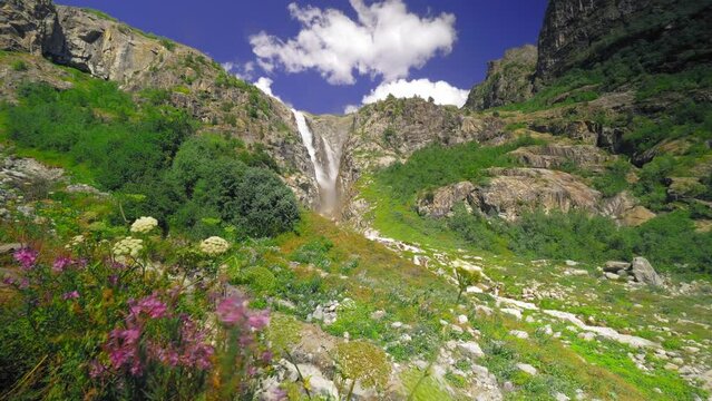 One of most beautiful waterfalls in Georgia waterfall Shdugra waterfall . tourist Attraction. mountain pink flowers grow on mountain, waterfall flows into river against background of blue sky. Summer.