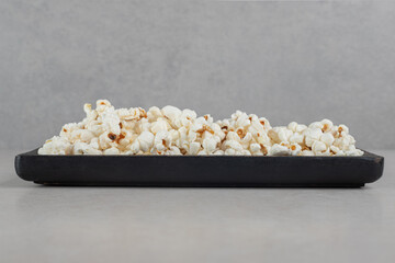 Black tray of popcorn on marble background