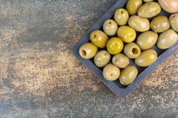 A dark board of some salty delicious olives on marble background
