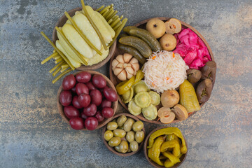 Salty vegetables in wooden bowls on marble background